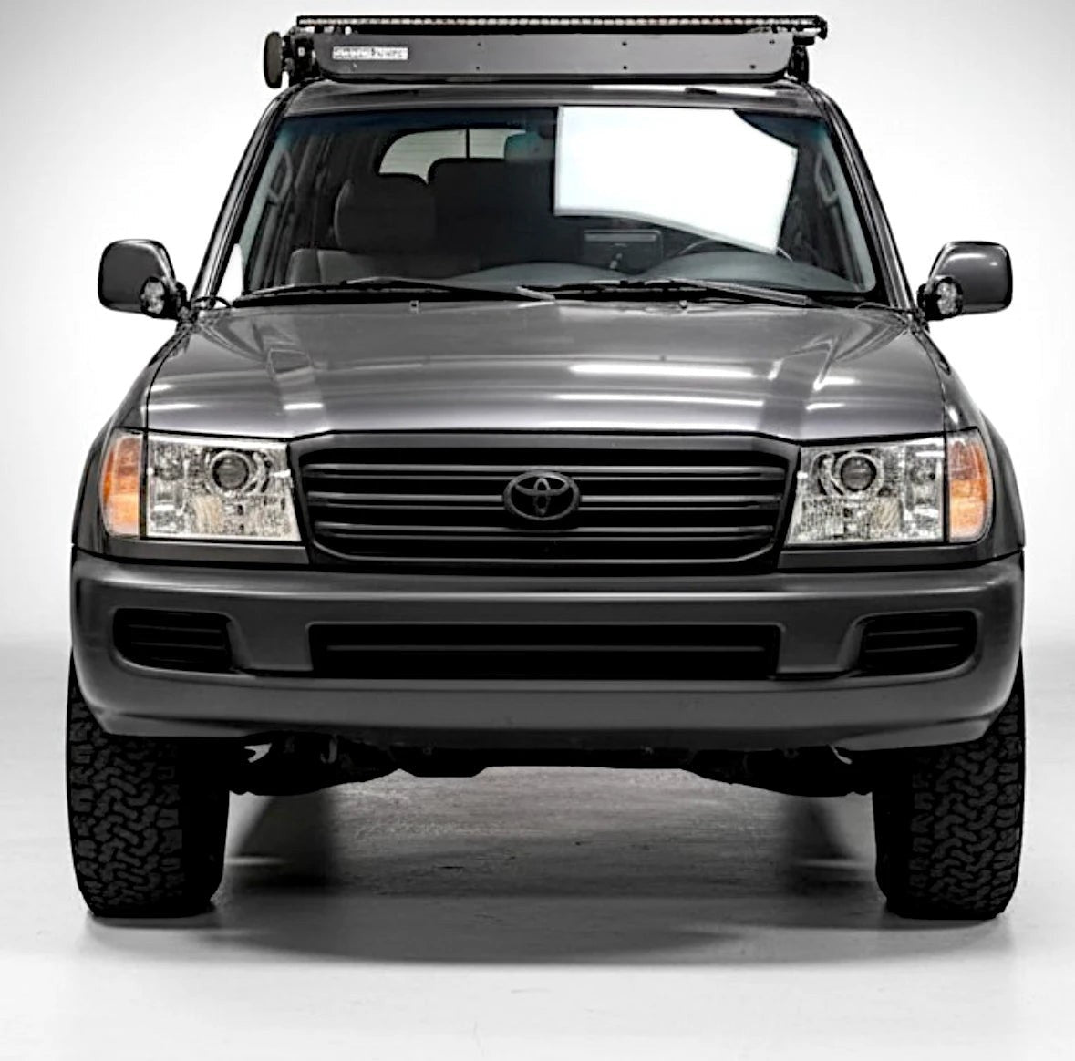 Ninja Cruiser LED projector headlights with glass lenses installed on a grey Toyota Land Cruiser 100 Series on studio background