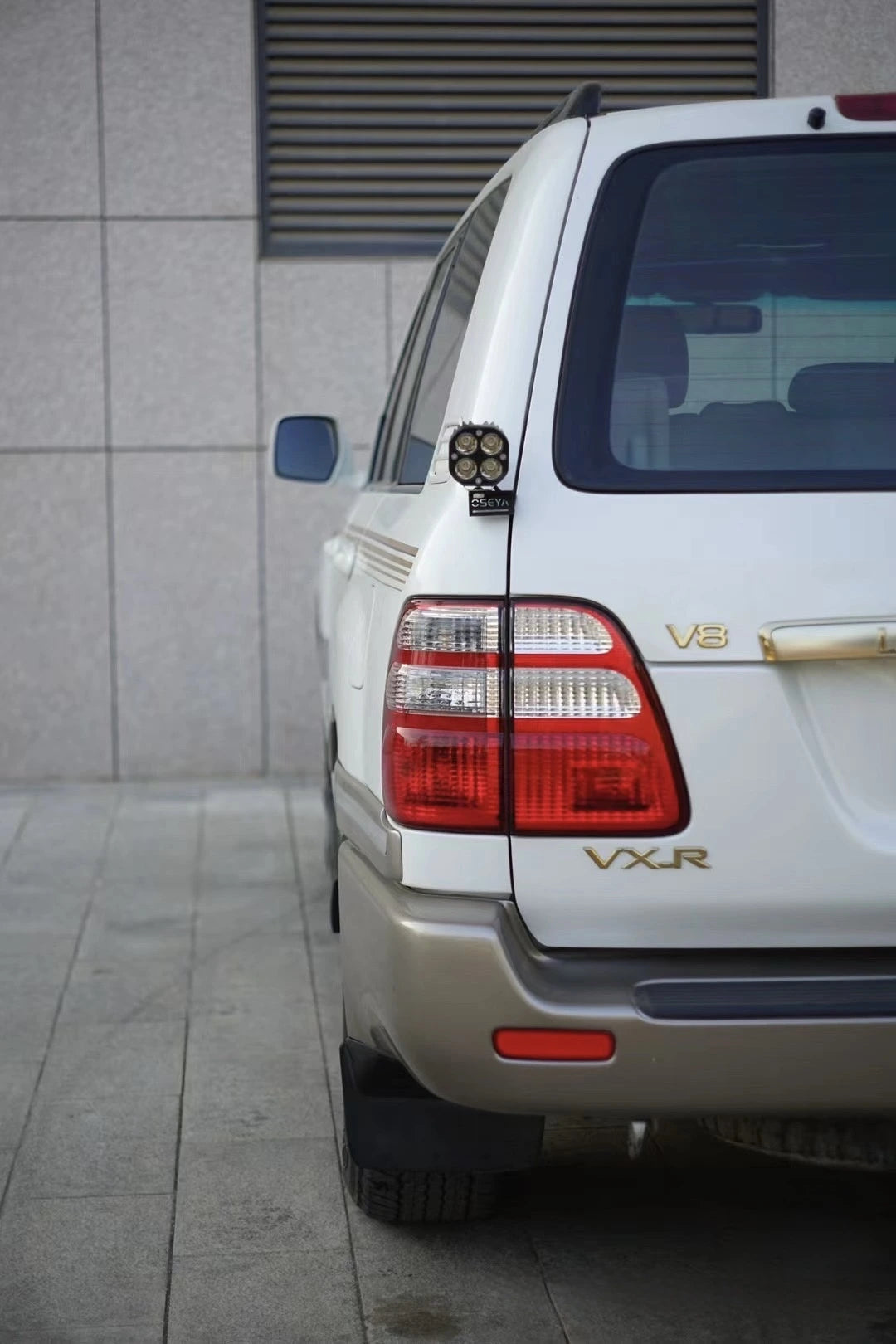 Toyota Land Cruiser 100 LC100 LX470 rear view with VXR badge showing aftermarket LED work light mounted on tailgate hinge bracket