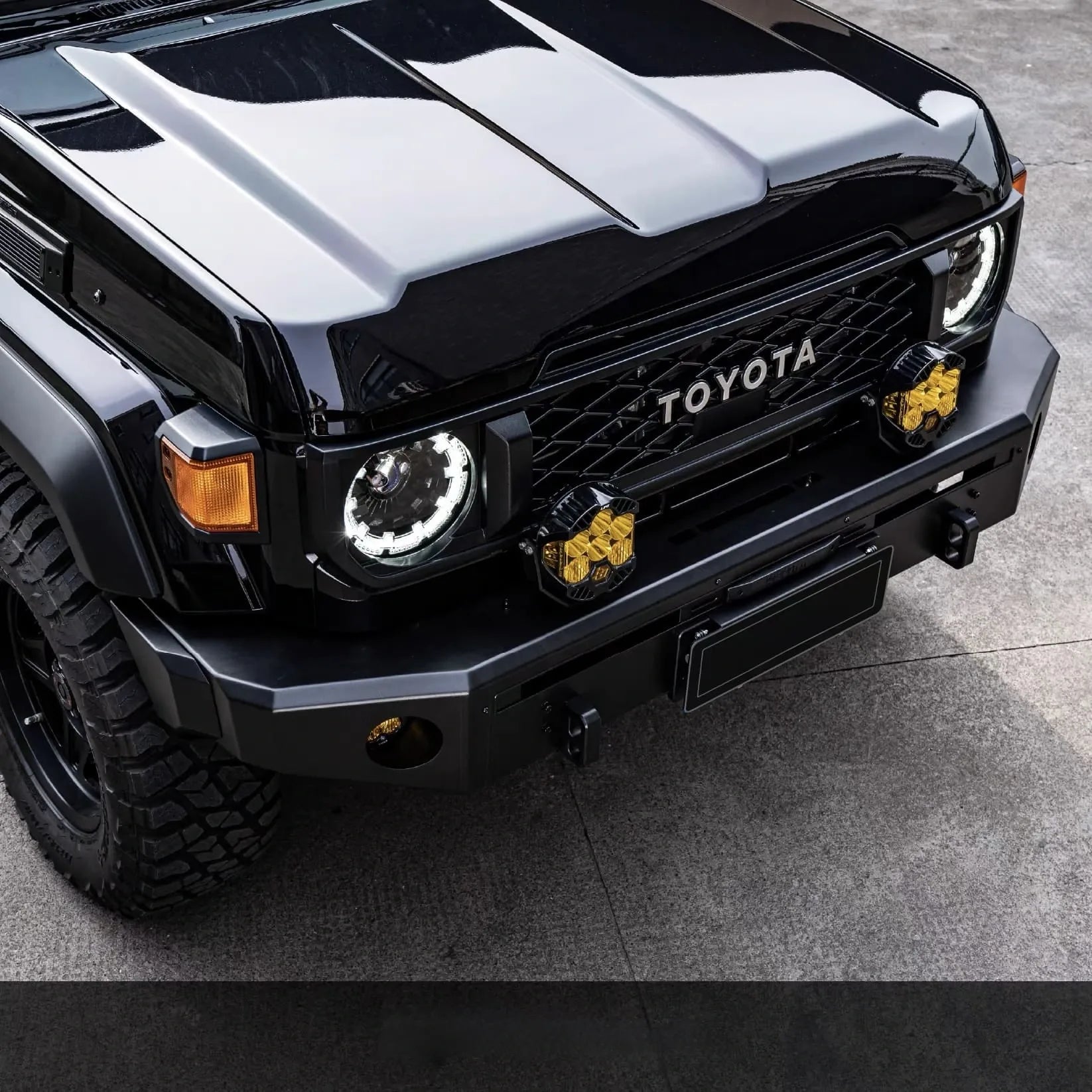 Front view of Black Toyota Land Cruiser 70 Series with yellow off-road led lights and off-road heavy duty front bumper on cement floor road