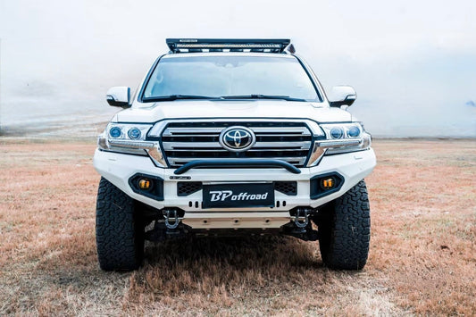 white suv toyota land cruiser lc200 with heavy duty white powder coated front bumper fitted 2 yellow fog lights and roof rack led light bar on dry grass pavement