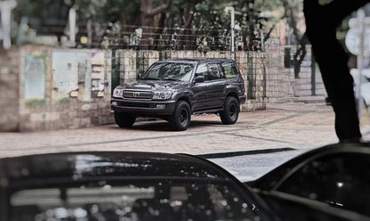 Front view of a black toyota Land Cruiser 100 Series showcasing LED projector headlight upgrade parking at the side of the road