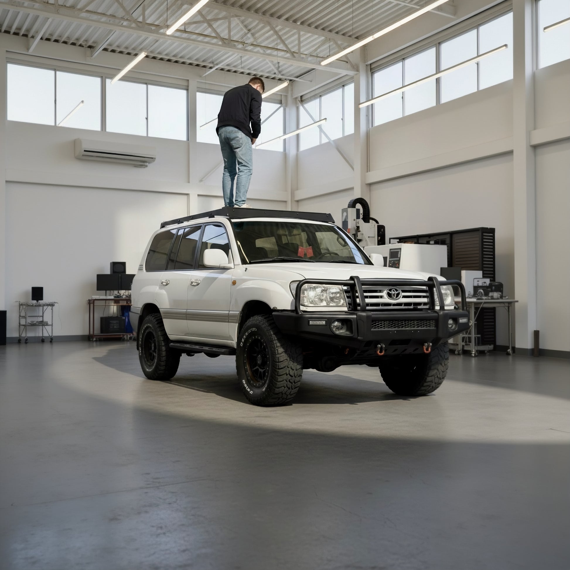 White Land Cruiser 100 series in a large indoor space with a person standing on top of the modular slim roof rack- sherpa style
