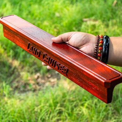 Hand holding a red wooden product with 'Land Cruiser' branding against a grassy background