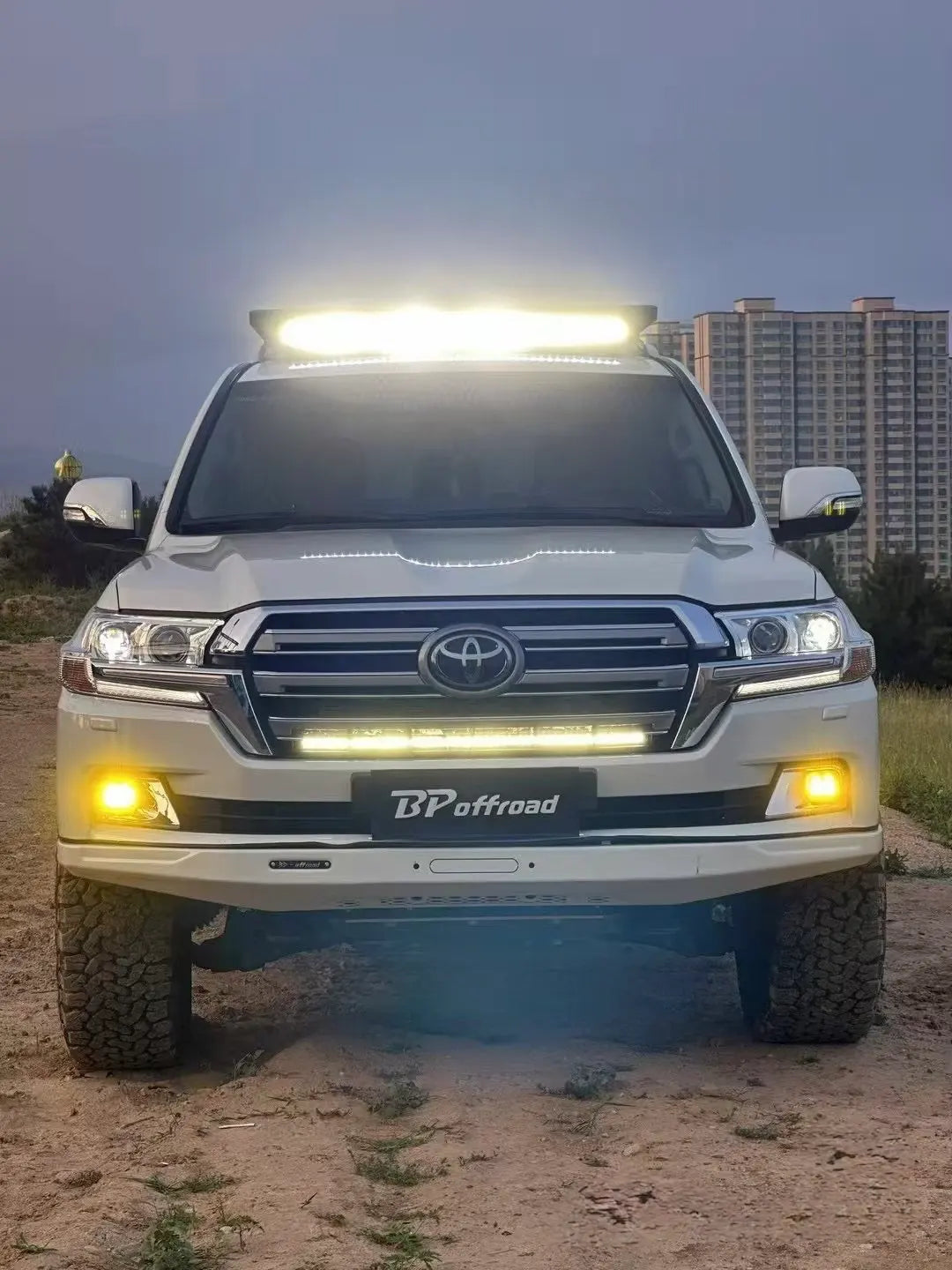 White facelift Toyota LC200 SUV with light bar fog light on a dirt road at dawn