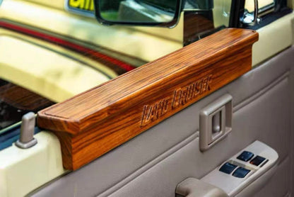 Land Cruiser 70 Series Solid Wood Door Armrest - Natural wood grain finish installed on the driver's side interior door, featuring carved "LAND CRUISER" text