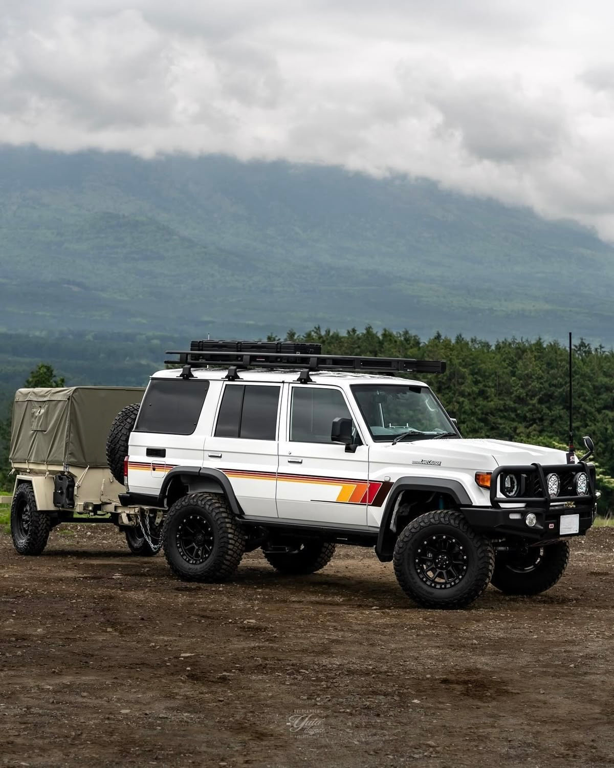 White Land Cruiser 76 wagon with a trailer on a dirt road with mountains in the background