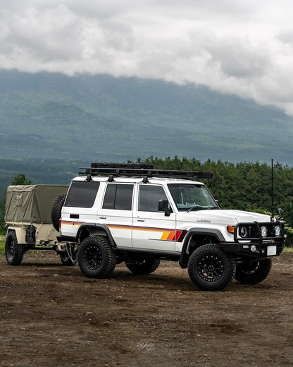 White Land Cruiser 76 wagon with a trailer on a dirt road with mountains in the background