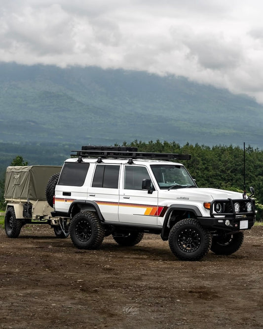 White Land Cruiser 76 wagon with a trailer on a dirt road with mountains in the background