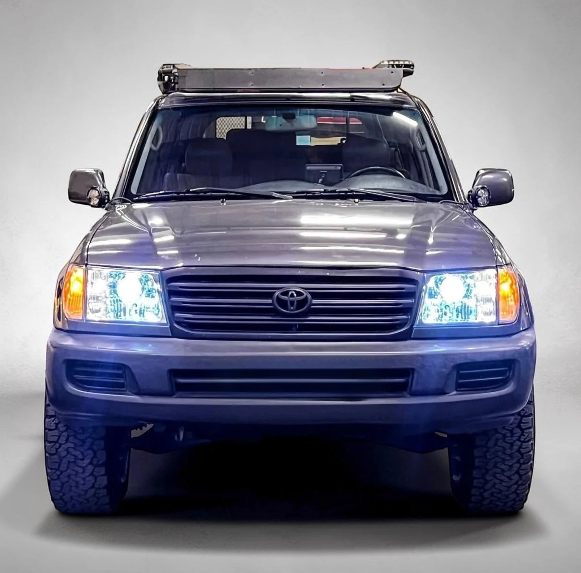Ninja Cruiser LED projector headlights switch on with blue lighting effect on a grey Toyota Land Cruiser 100 Series with studio background