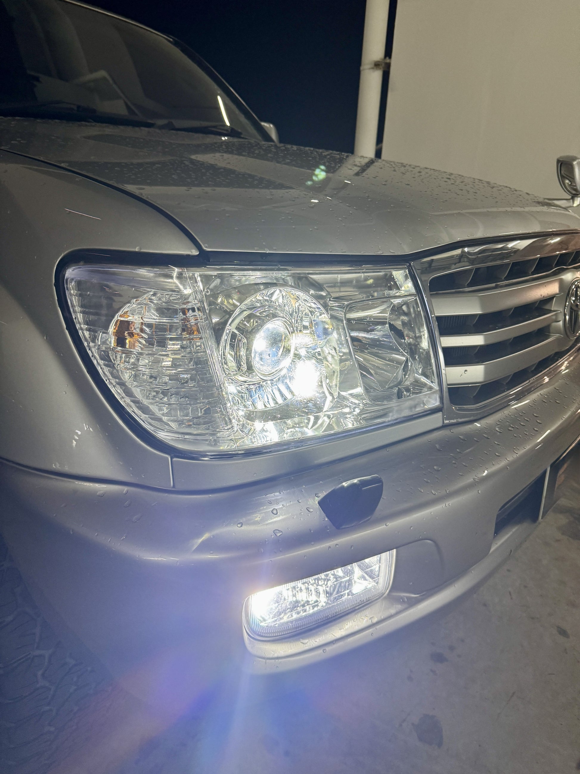 Close-up of a a LC100 front headlight and bumper fog light at night with white light